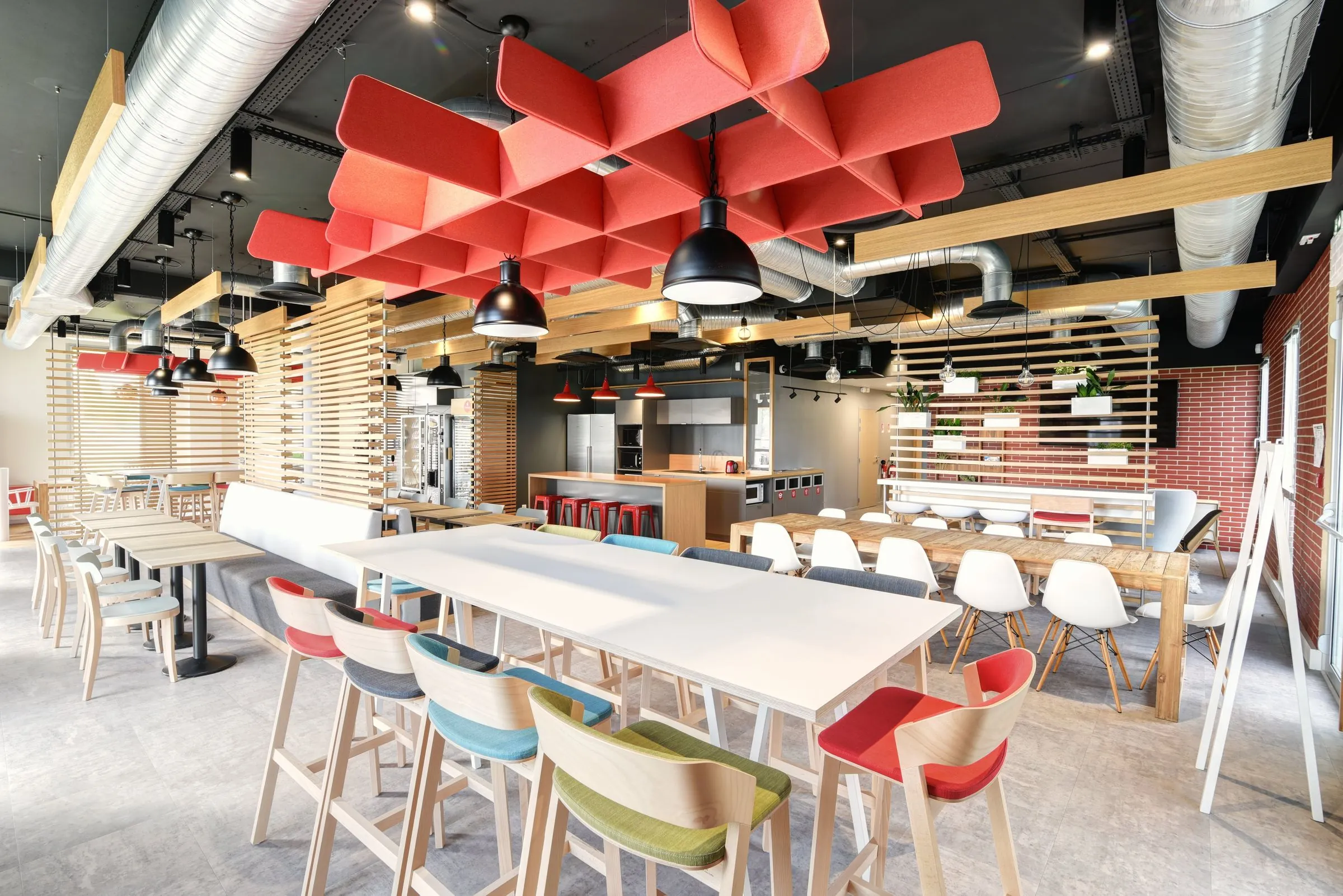 Espace de restauration d’entreprise lumineux, plafond acoustique rouge et mobilier bois