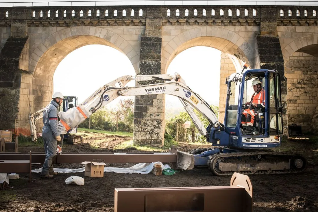 Mini-pelle en action sous les arches d’un pont en pierre