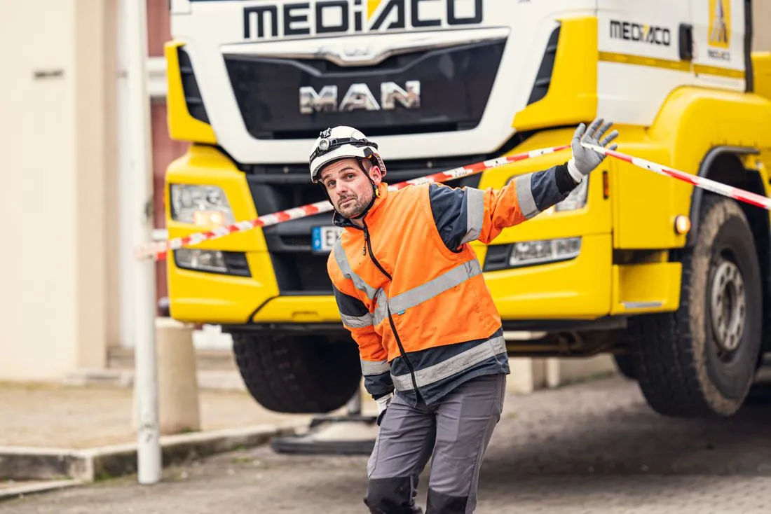 Technicien en gilet orange guidant un camion Mediaco
