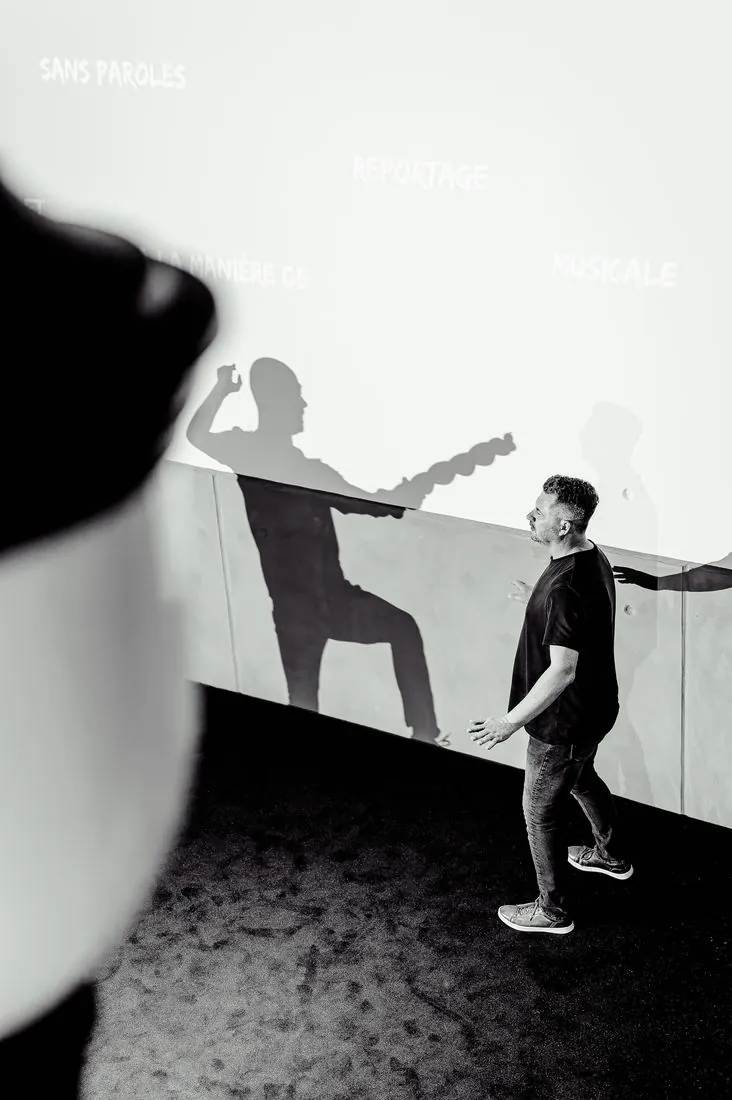 Silhouette d’un intervenant projetée sur un mur blanc, en noir et blanc
