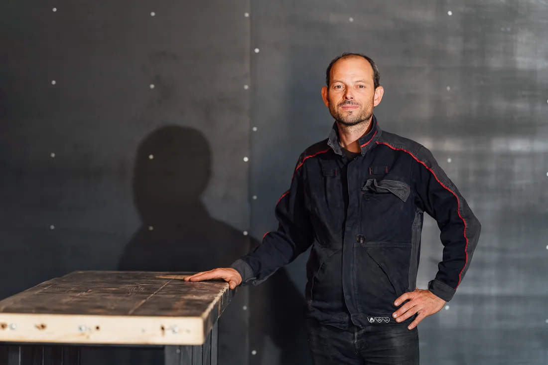 Portrait d’un artisan en veste de travail, main posée sur un établi en bois, dans son atelier