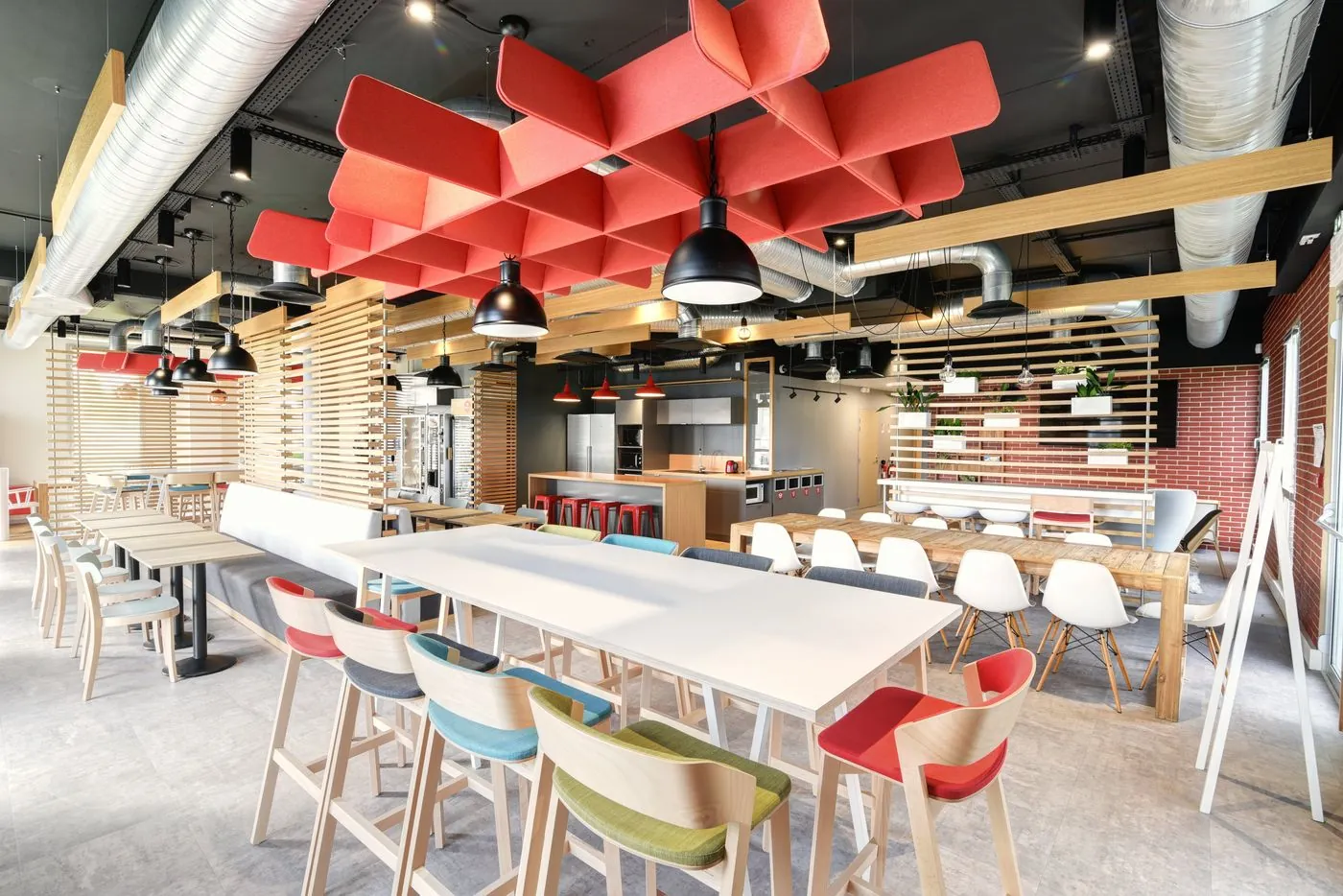 Espace de restauration d’entreprise lumineux, plafond acoustique rouge et mobilier bois